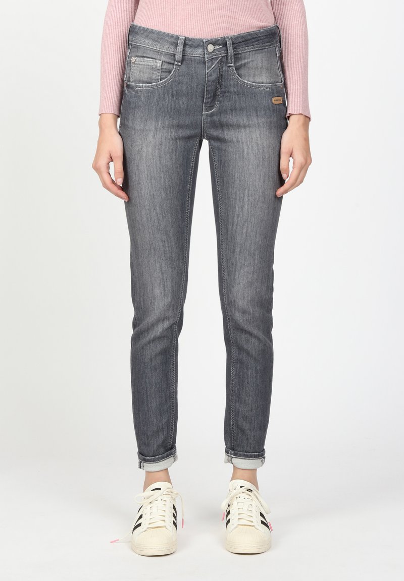 Graue Jeans aus Denim mit slim fit, fünf Taschen, umgeschlagenen Säumen und leichter Abnutzung; kombiniert mit weißen Sneakern mit schwarzen Streifen.