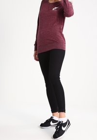 Bordový mikin s dlouhým rukávem a kulatým výstřihem, s malým bílým logem, zkombinovaný s černými slim-fit džíny a černými teniskami s bílými detaily.