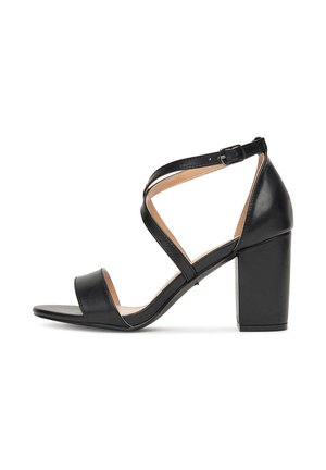 Sandale en cuir noir avec un talon épais et carré, dotée de brides croisées et d'une fermeture à boucle. Texture lisse et design à bout ouvert.