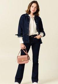 Tumma farkkutakki, valkoinen nappipaita, tummansiniset levenevät farkut, pitää vaaleanpunaista käsilaukkua, jossa on kultainen solki, ja valkoisia tennareita.