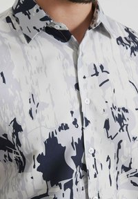 Chemise à manches courtes avec un motif abstrait blanc et bleu marine, dotée d'un col pointu, de boutons et d'une texture lisse.