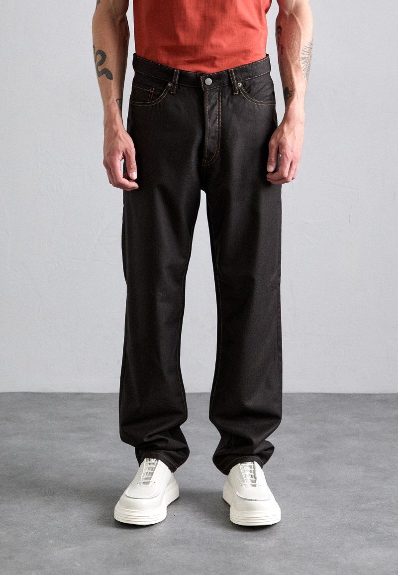 Black denim jeans with a straight-leg fit, featuring contrast stitching and a classic five-pocket design. Paired with white sneakers.