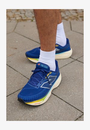 Blue athletic shoes with mesh upper, features reflective accents, white laces, and a cushioned sole in multiple colors. Worn with white socks.