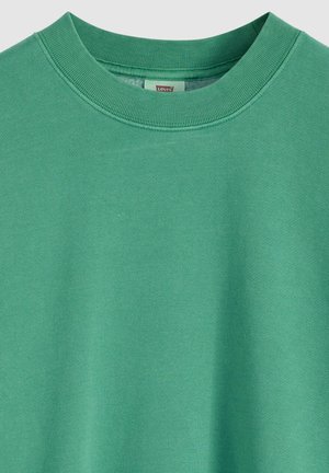 Vihreä puuvillainen collegepaita, jossa on pyöreä kaula-aukko, resorireunus ja sileä pinta, painottaen yksinkertaisuutta ja mukavuutta.