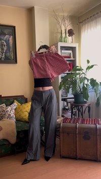 Un short en vichy rouge et blanc suspendu sur un cintre, mettant en valeur une taille froncée, avec un pantalon large gris et des chaussures noires à bouts pointus en arrière-plan.