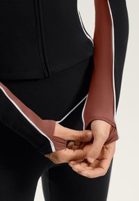 Schwarzes und kastanienbraunes Langarmoberteil mit weißen Nähten; verfügt über Daumenlöcher und eine enganliegende Passform, zeigt eine glatte, dehnbare Stofftextur.