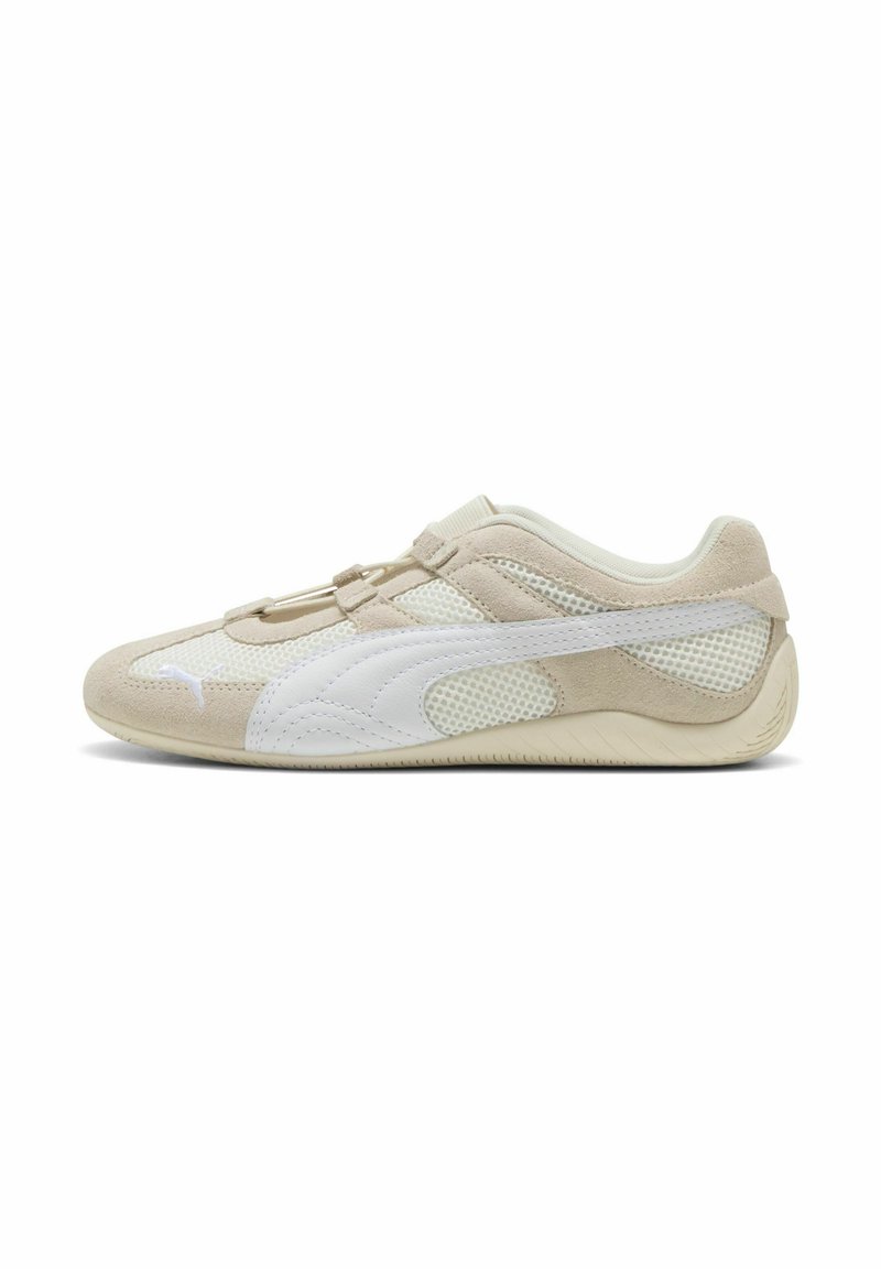 Zapatilla deportiva beige y blanca con parte superior de ante y malla, puntera redondeada, cierre de cordones elásticos y suela texturizada para mayor agarre.