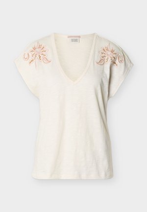 Kremasta kratka majica z V-izrezom, okrašena z rožnim vezenjem v roza in zlati barvi na ramenih, izdelana iz lahkega, rahlo teksturiranega blaga.