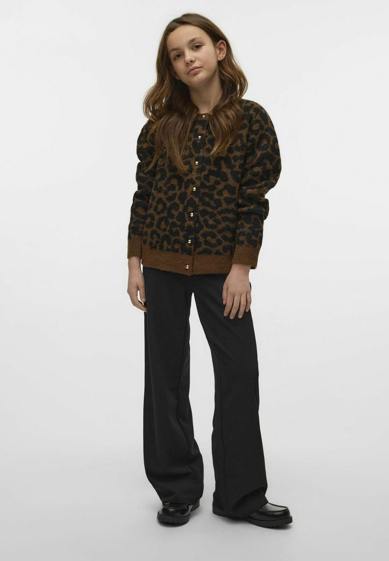 Kardigan i leopardmönster i mörkbrun och svart ull med guldfärgad knäppning, ihopparad med lösa svarta byxor och svarta skor.