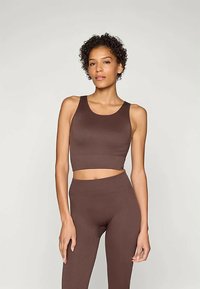 Barna bordázott, rövid fazonú felső és hozzáillő, magas derekú leggings. Sima textúra, testhezálló fazon, széles vállpántok és elasztikus derékpánt.