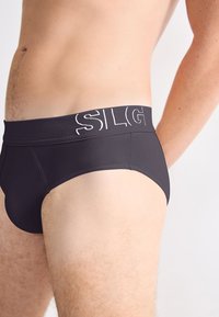 Schwarze Brief-Unterwäsche mit breitem Bund und weißer Schrift. Hergestellt aus glattem Material mit enger Passform.