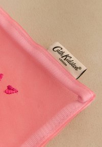 Pungă din material roz, cu o suprafață texturată, având accente brodate în formă de inimă și un eticheta vizibilă cu inscripția "Cath Kidston London."