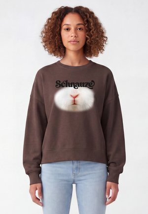 Frau mit lockigem Haar, die einen braunen Pullover trägt, zeigt eine Nahaufnahme von der Nase und dem Mund eines weißen Kaninchens mit dem Wort "Schnauze" darüber.