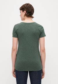 Grøn kortærmet t-shirt med rund halsudskæring, blød tekstur og diskrete stænk; stylet med lige snit denim jeans.