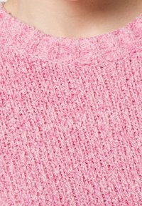 Texturovaná růžová pletená svetr látka, která má žebrovaný výstřih, s měkkým, chmýřovým vzhledem a různou tloušťkou stehů.