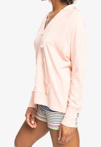 Felpa con cappuccio rosa chiaro, con scollo a V, dettaglio con cordino e maniche lunghe, abbinata a pantaloni corti multicolori a righe orizzontali.