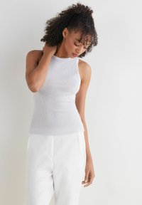 Witte geribde tanktop met een hoge halslijn en aansluitend ontwerp, gecombineerd met witte broeken. De stof lijkt glad met een subtiele textuur.