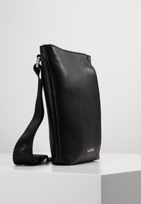 Černá kožená taška přes rameno s texturovaným povrchem, elegantním designem, nastavitelným popruhem a jemným logem na přední straně.