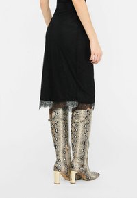 Zwarte rok met kant overlay en een golvende zoom, gecombineerd met kniehoge metallic laarzen met slangenprint, voorzien van blokhakken en zijgespen.