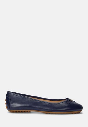 Ballerine en cuir bleu marine avec un petit nœud à l'avant et des grips en caoutchouc marron sur la semelle et le talon.
