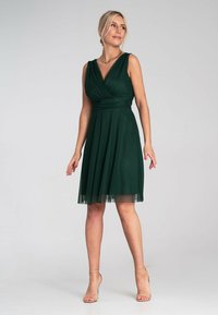 Grünes ärmelloses Kleid mit V-Ausschnitt, plissiertem Rock und transparenter Saumverarbeitung. Hergestellt aus weichem Stoff, hat es eine taillierte Taille und eine fließende Silhouette.