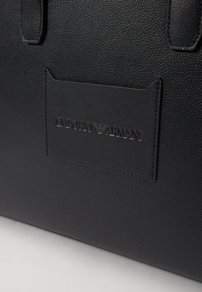 Svart läder tote-väska med texturerad yta, prydd med ett märke som har det präglade varumärket "EMPORIO ARMANI." Släta, robusta handtag.