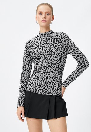 Maglietta a maniche lunghe con collo alto grigia con stampa leopardata nera; design aderente, texture morbida e collo alto, abbinata a una gonna plissettata nera.