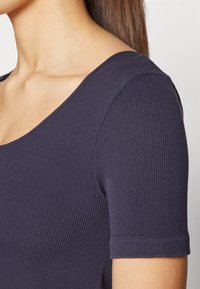 Marinblå ribbestrikket topp med bred scoop-hals og korte ermer, med teksturert stoff og tettsittende silhuett.