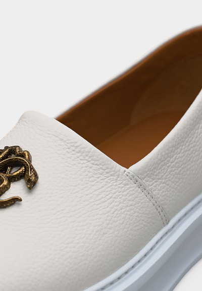Λευκό παπούτσι από υφή δέρματος με κεντημένο μπρονζέ εμβληματικό φίδι στο πάνω μέρος και εσωτερική επένδυση σε ανοιχτό καφέ χρώμα.