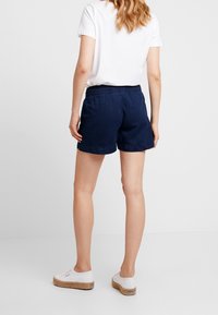 Shorts en coton bleu marine avec une taille élastique, finitions sur les côtés et une coupe décontractée. Associés à des espadrilles en toile blanches.