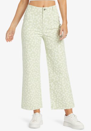 Groene wijde broek met witte bloemmotief, hoge taille, twee voorkeuzes en een cropped fit, gecombineerd met witte sneakers.