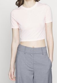 Kvinna som bär en ljusrosa kortärmad Nike-t-shirt och höga grå ränderbyxor med händerna delvis i fickorna.