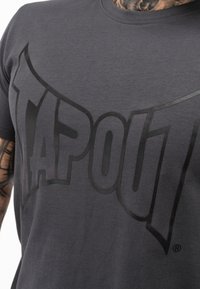 Sötétszürke pamut póló, melynek elülső részén egy nagy fekete "TAPOUT" logó található. Az anyag sima, klasszikus kerek nyakú dizájnnal.