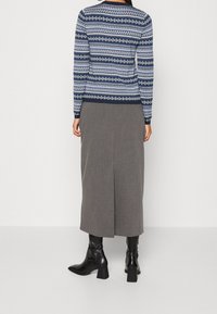 Pull à motifs bleu marine à manches longues, associé à une jupe longue grise avec une fente au dos, et des bottines noires à talon bloc.