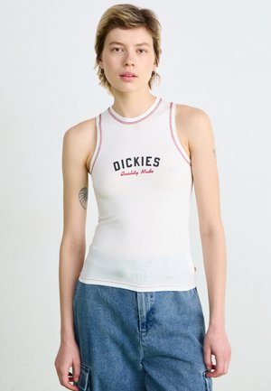 Débardeur sans manches blanc avec des coutures rouges et le texte noir "DICKIES", présentant une coupe ajustée et un col rond. Pantalon en denim en arrière-plan.