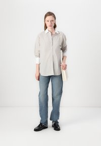 Gestreepte blouse met pofmouwen, gecombineerd met lichtblauwe jeans en zwarte loafers. Accessoires zijn een crèmekleurige handtas.