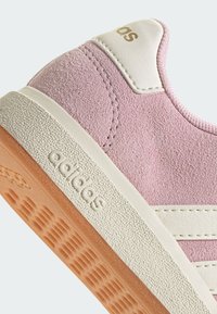 Sneaker en daim rose avec des accents en cuir blanc, semelle en caoutchouc crème clair texturée, et marquage doré au niveau du talon. Design à profil bas.