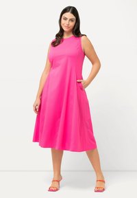 Vaaleanpunainen sleeveless-mekko, jossa on leveä helma ja sivutaskut. Silkkinen, kevyt kangas ja pyöreä pääntie. Yhdistetty hihnatossuihin.