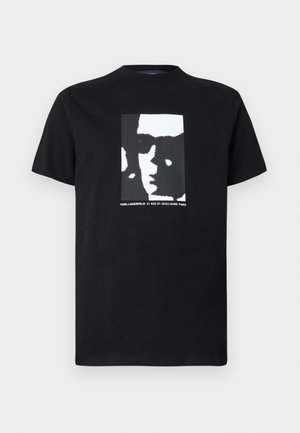 T-shirt preto em algodão com um gráfico central de um rosto em tons de branco e cinza, com texto abaixo em fonte branca. Decote clássico em crew.