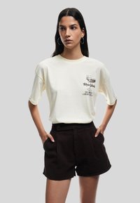 Lys gul oversized T-shirt med grafisk print; parret med højtaljet sorte shorts; korte ærmer, afslappet pasform og rund halsudskæring.