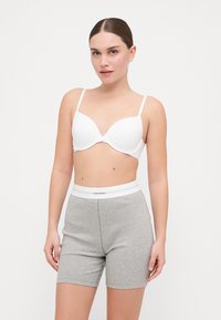 Hvit polstret BH med tynne stropper, sammen med grå bomullsshorts med en hvit midjebånd som har "Calvin Klein"-logo. Glatt finish.
