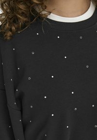 Sweatshirt nero con dettagli metallici sparsi e decorazioni. Materiale morbido con scollatura rotonda e polsini a costine.