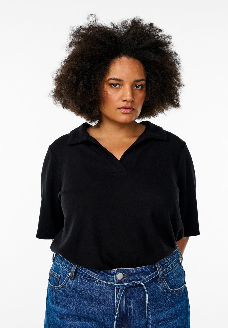 Svart polo skjorta med krage och korta ärmar, matchad med högmidjade blå denimjeans. Slät tygtextur, enkla linjer.