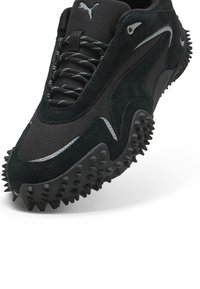 Sneakers Puma in suede nero e mesh, con suola in gomma chiodata, punta arrotondata e dettagli riflettenti lungo i lati.