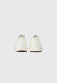 White sneakers with a smooth, matte finish, featuring a gray pull tab at the heel and a light beige rubber sole. Minimalist design.