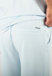 Ensemble de pyjama bleu clair avec un motif en texture et en gaufré. Dispose d'une poche arrière et d'une petite étiquette "Hollyghost" au niveau de la taille.