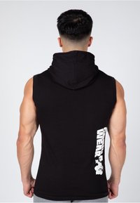 Black sleeveless hoodie with a large white graphic on the side, featuring text and an illustrated design. Fabric appears soft and textured.