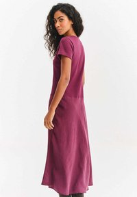 Bordowa sukienka maxi z krótkimi rękawami, gładką fakturą i subtelnymi rozcięciami po bokach, o luźnym fasonie i minimalistycznym designie.