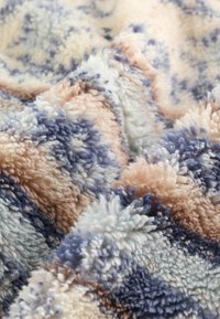 Blød, fluffy stof med et struktureret, multicolor mønster i nuancer af blå, beige, hvid og brun, vist i nærbillede af folder.