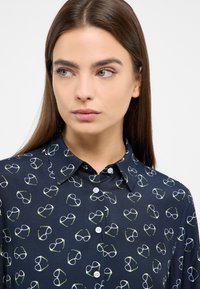 Navy-blaues Hemd mit Knöpfen, das ein Muster aus weißen und grünen Brillen zeigt. Glattes Material mit einem Kragen und sanftem Glanz.